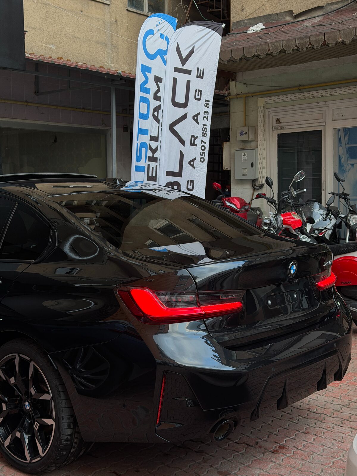 Black Garage tabelası önünde bekleyen siyah BMW